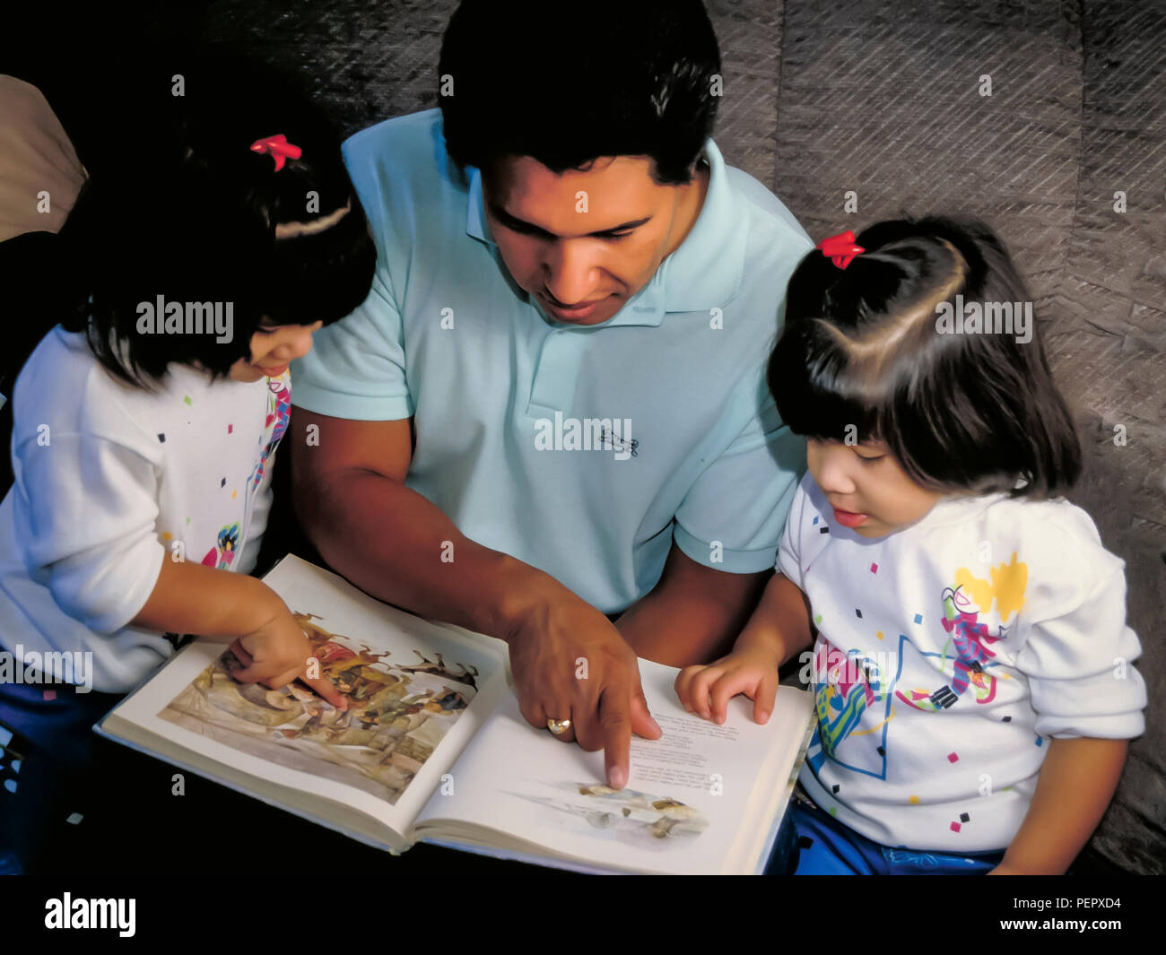Mexican heritage dad reading storybook together with twin daughters sisters.  MR   © Myrleen Pearson  ...Ferguson Cate Stock Photo
