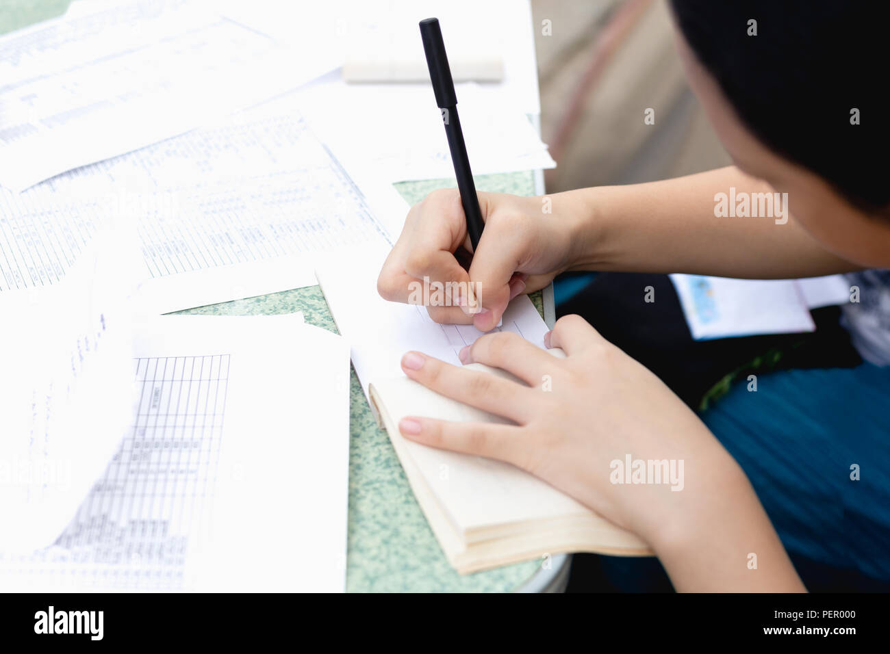 Schoolgirl with pen writing down doing homework on the table. Stock Photo