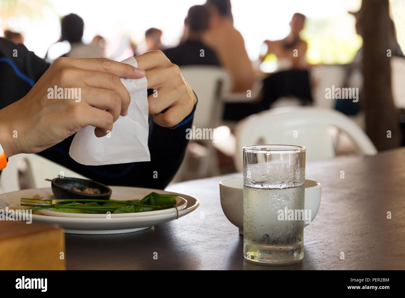 Hand using white tissue paper after finish lunch with glass of water on