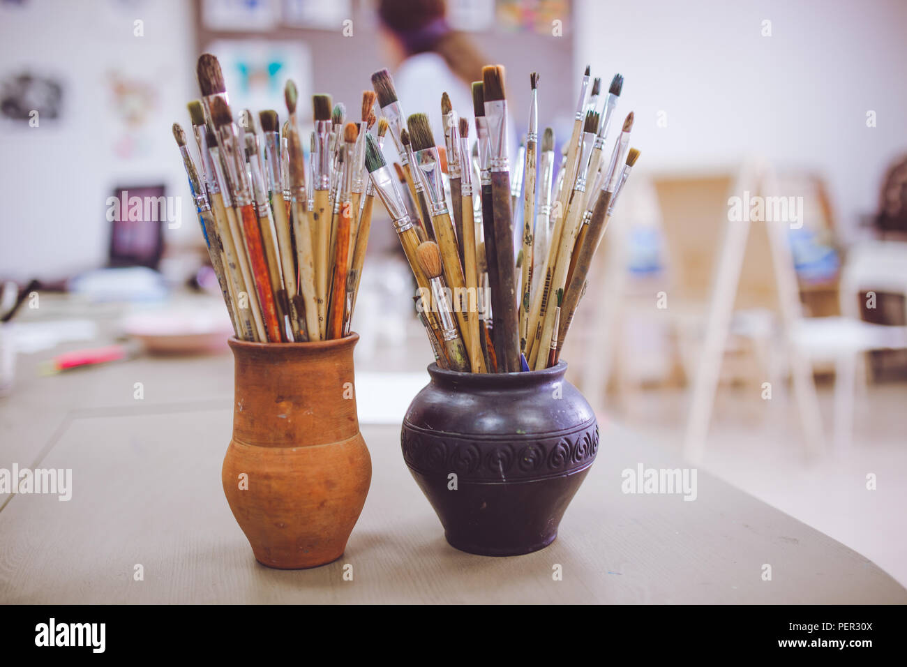 A bunch of art brushes standing in ceramic vases, on the table in the art studio. Stock Photo