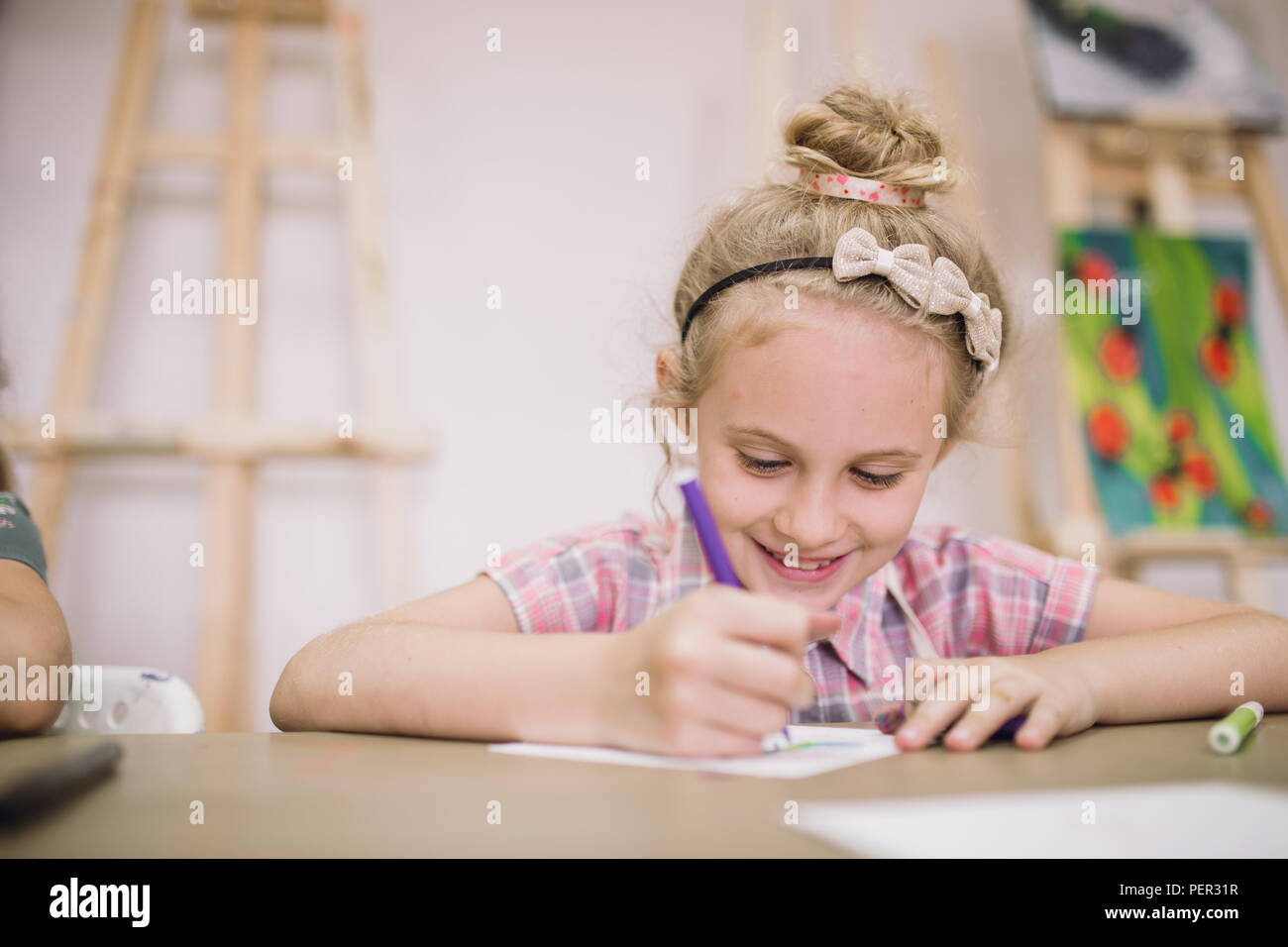 Blonde cute smiling seven-year-old girl, draws at the table in the creative studio. Stock Photo