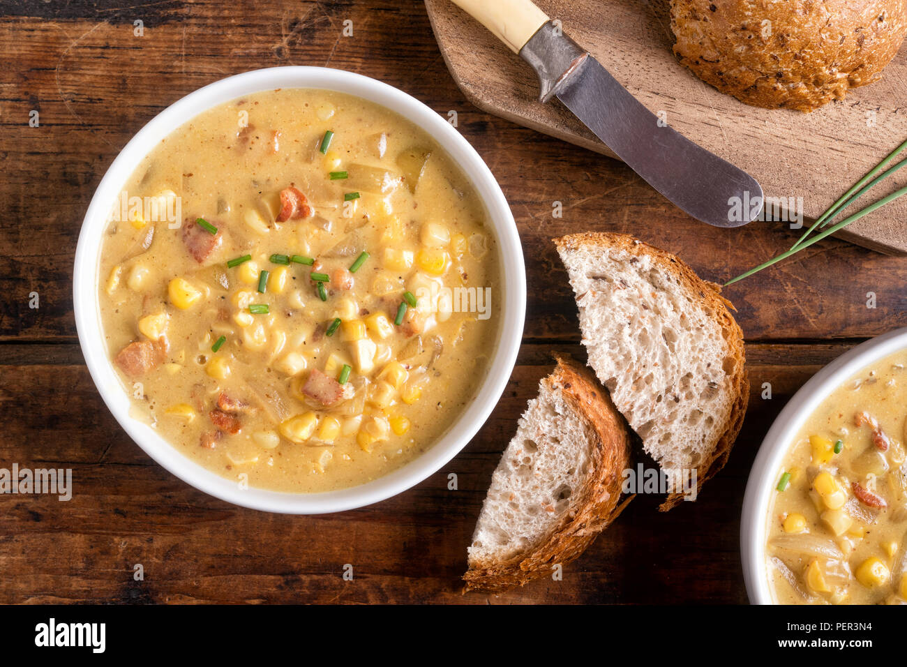 A bowl of delicious homemade bacon corn chowder with whole grain bread on a rustic wood table top. Stock Photo