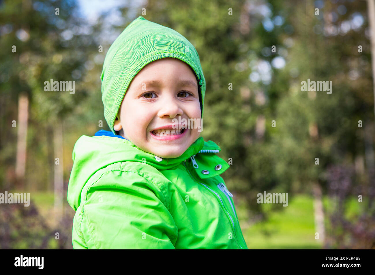 Charming child kid boy in green clothes outdoors in the park. Smiling face. Stock Photo