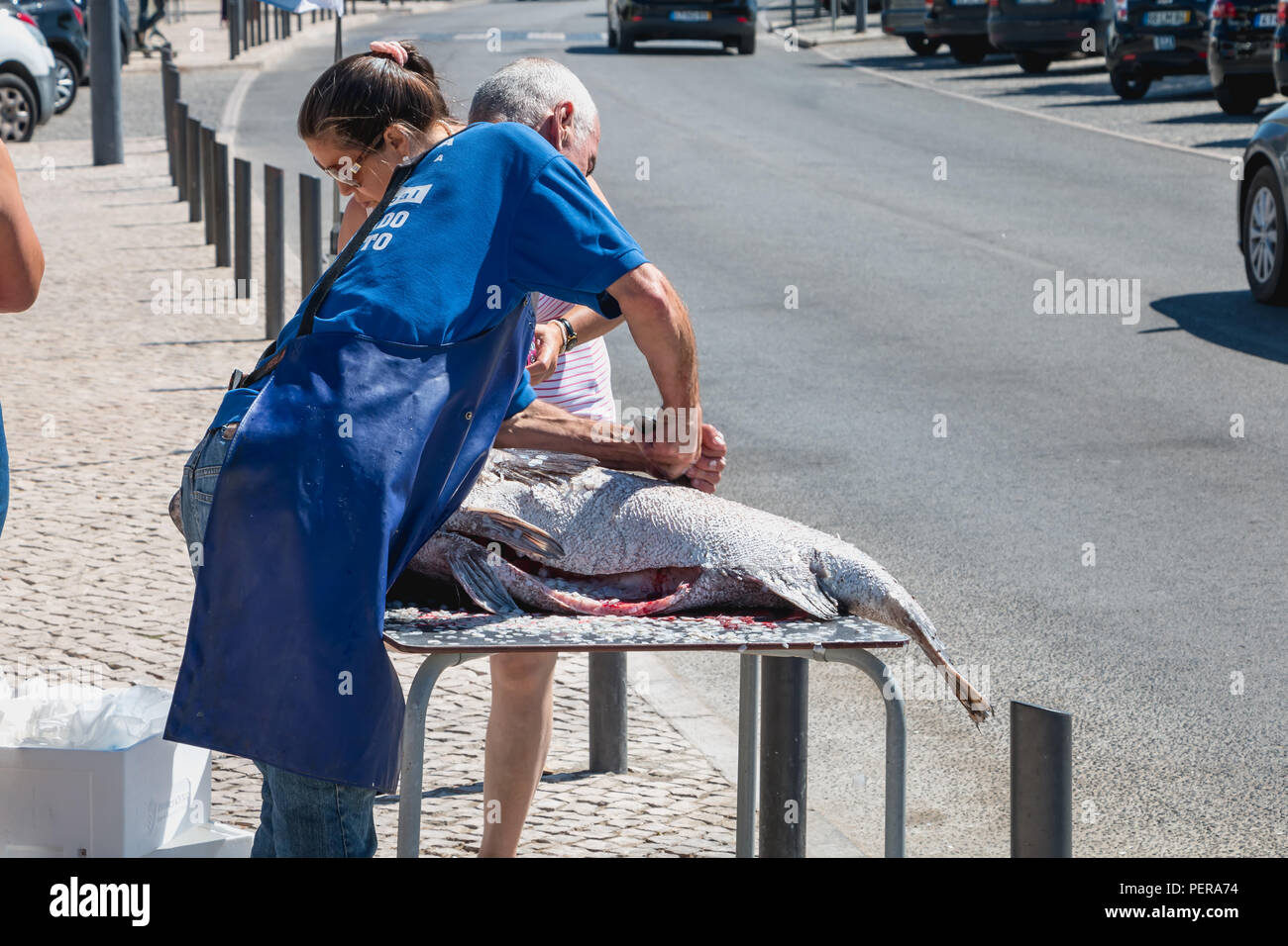 Setubal, Portugal - August 8, 2018: Man who removes the scales of a big fish in the street in front of a restaurant on a summer day under the eyes of  Stock Photo