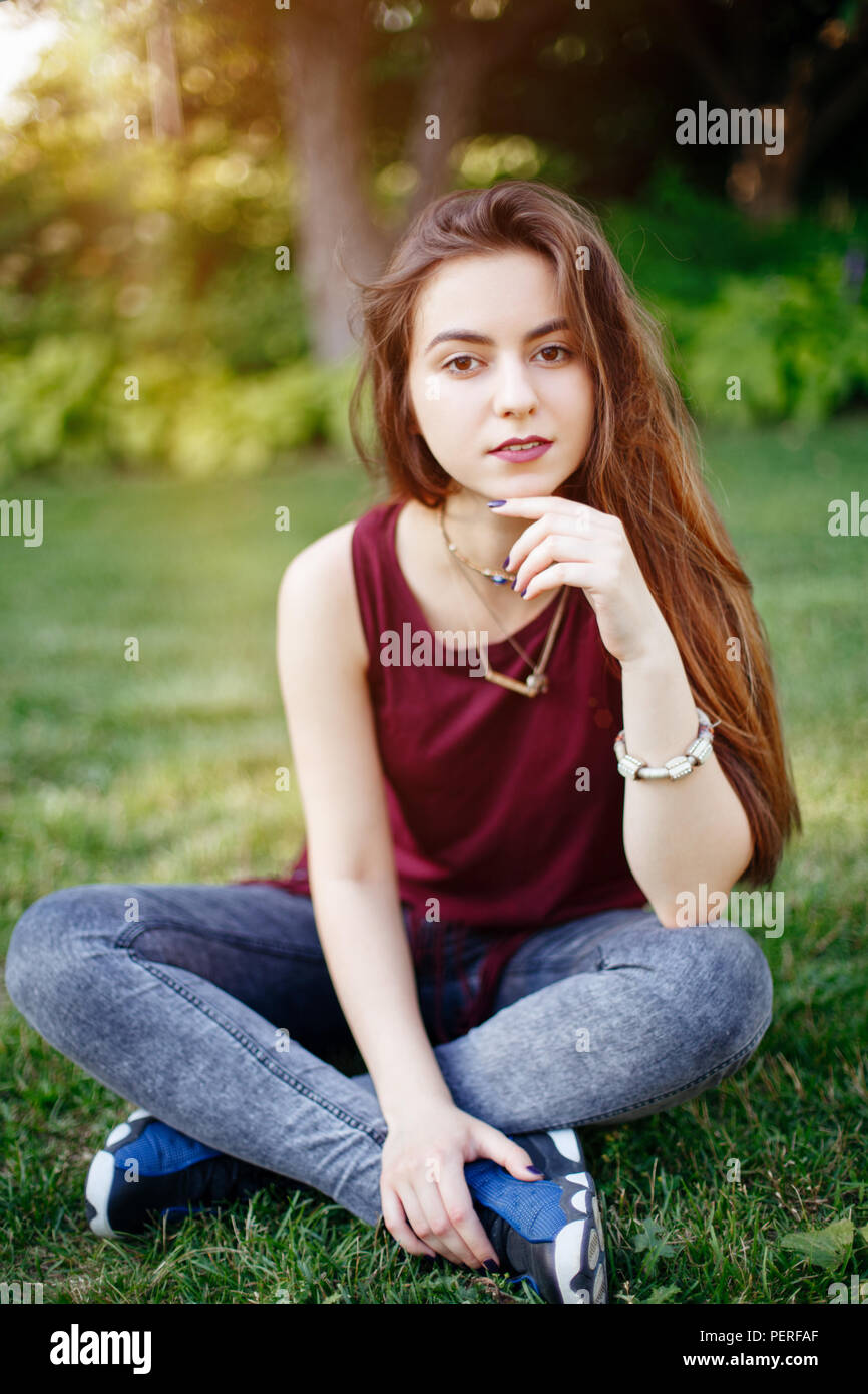 Portrait of beautiful pensive young Caucasian woman with long red hair in  red t-shirt and jeans sitting on grass in park meadow. Summer sunset with li  Stock Photo - Alamy