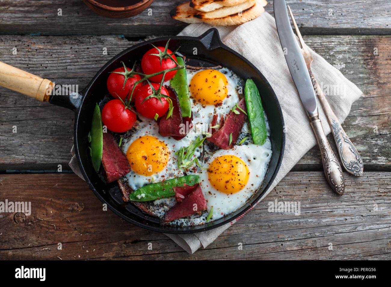 Fried eggs in a frying pan with cherry tomatoes, green peas and pastrami. Copyspace Stock Photo
