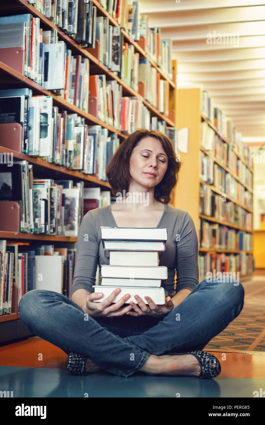 Portrait of tired middle age mature woman student sitting in library with closed eyes meditating, sleeping, teacher librarian profession, back to scho Stock Photo