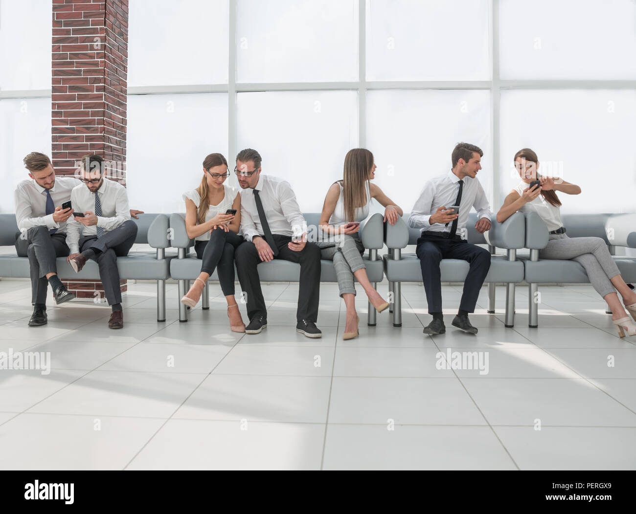 group of employees use smartphones while sitting in the office lobby ...