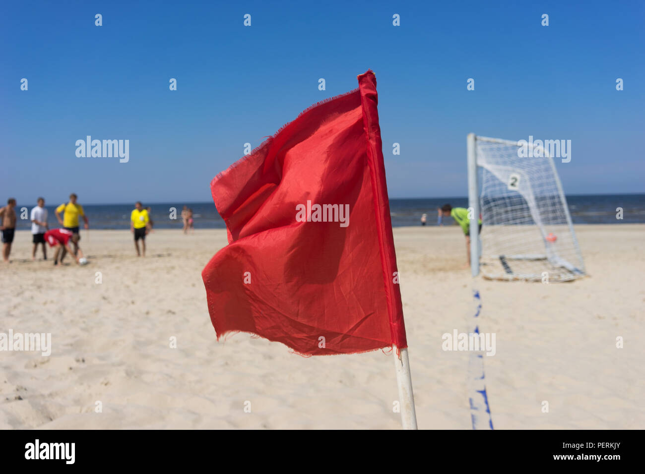 People Play Football On The Beach On A Background Of Red Flag