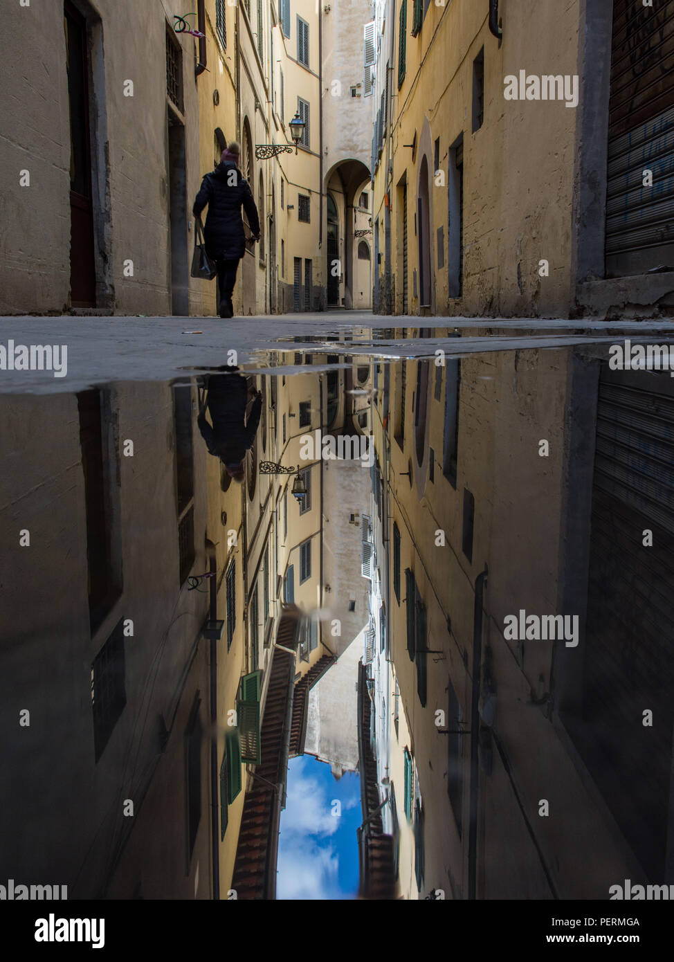 Florence, Italy - March 30, 2018: A pedestrian walks past traditional closely-built Renaissance-era houses reflected in a puddle on a street in Floren Stock Photo