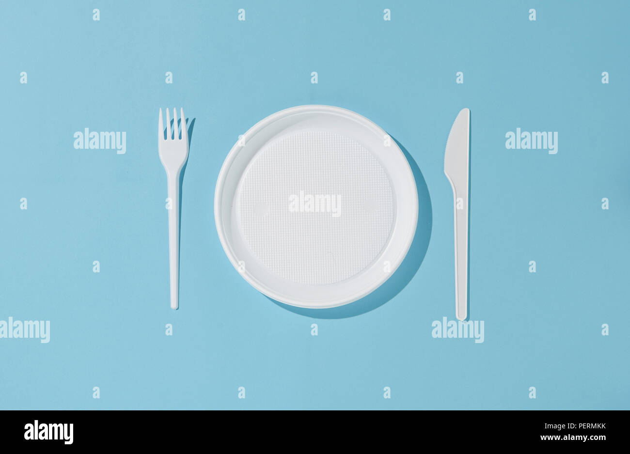 White plastic plate, knife and fork on a blue background. Plastic tableware. Stock Photo