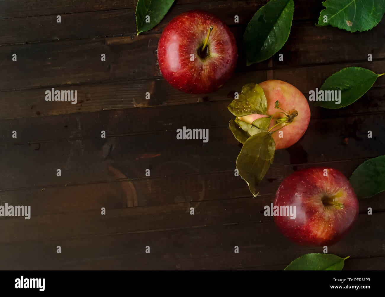 Two red apples with one yellow pink apple and leaves on wooden background.Copyspace left. Stock Photo