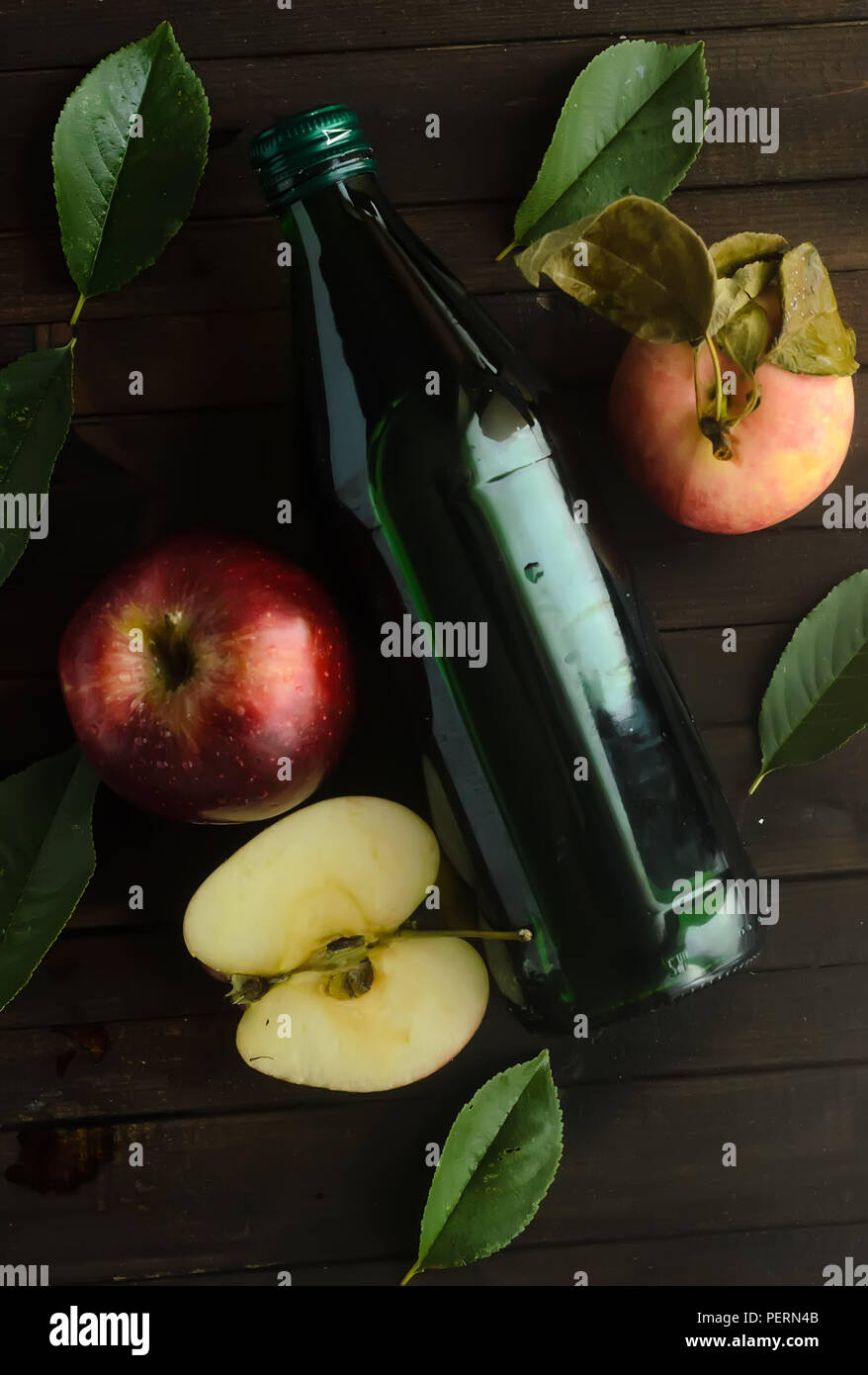 A bottle of a apple cider vinegar with fresh apples and green leaves on wooden background. Stock Photo