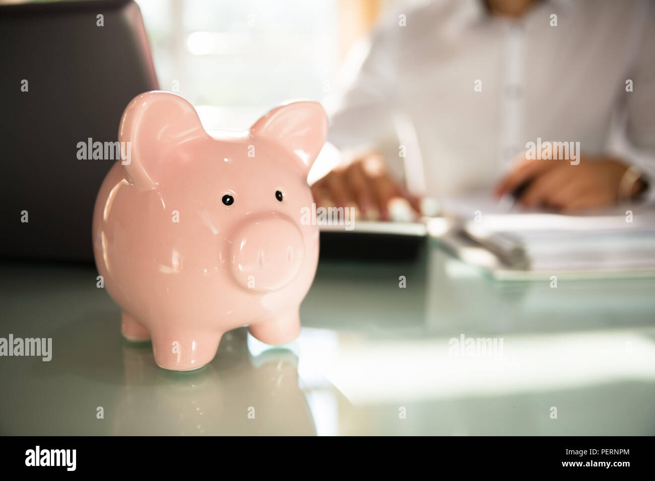 Close-up of a piggybank in front of businessman calculating bill with calculator Stock Photo