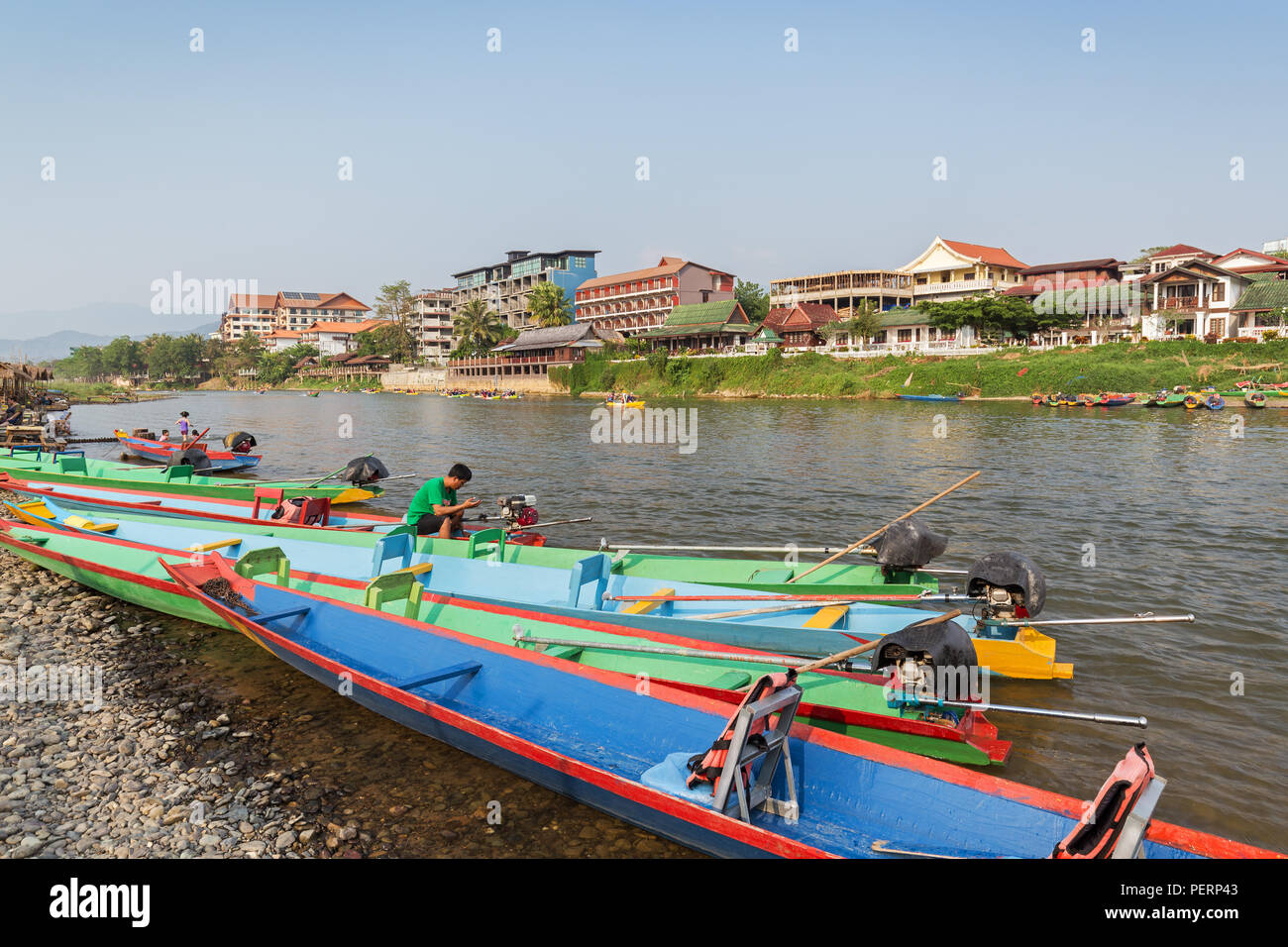 Colorful motoboats and few people on the Nam Song River and hotels in Vang Vieng, Vientiane Province, Laos, on a sunny day. Stock Photo