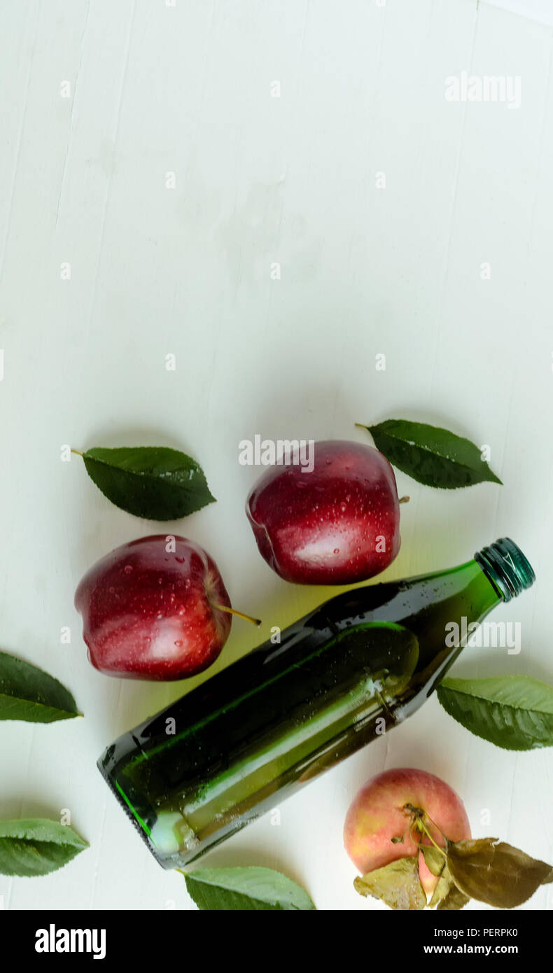 A bottle of a apple cider vinegar with three fresh apples and green leaves on white background.Copyspace top. Stock Photo