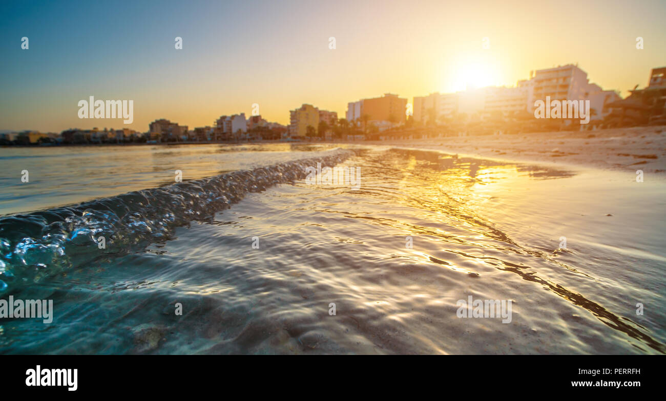 Wavy curves  of  sea is covered  in golden sunset light. Sea at sunset sunlight. Wavy curves pattern on beach.   Waves in bokeh focud Stock Photo