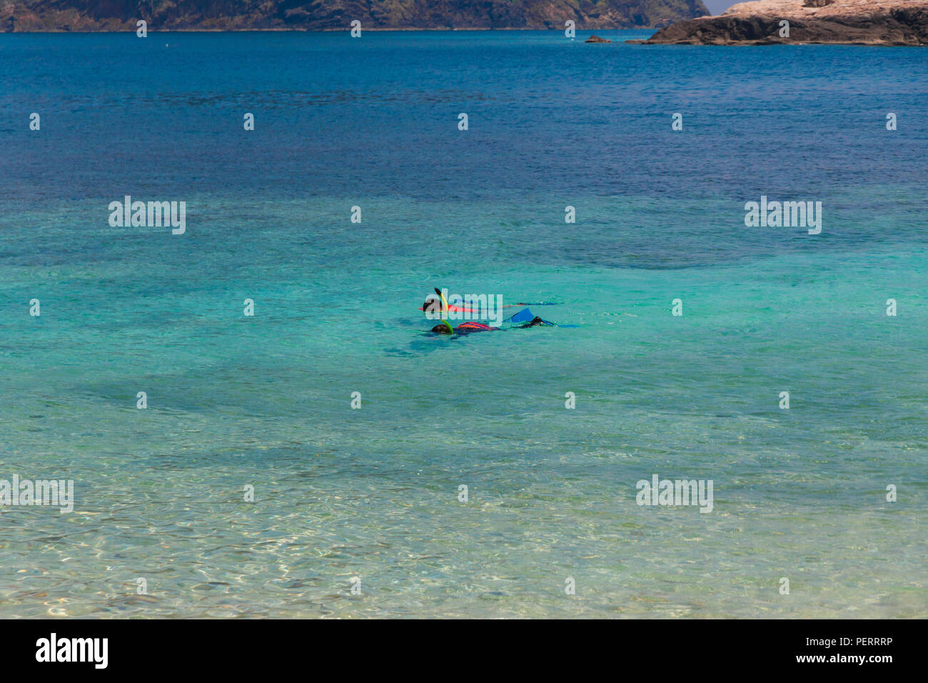Two tourists snorkelling in the turquoise blue sea, in front of the shallow clear waters of Rawa beach, an island near Perhentian Kecil in Malaysia. Stock Photo