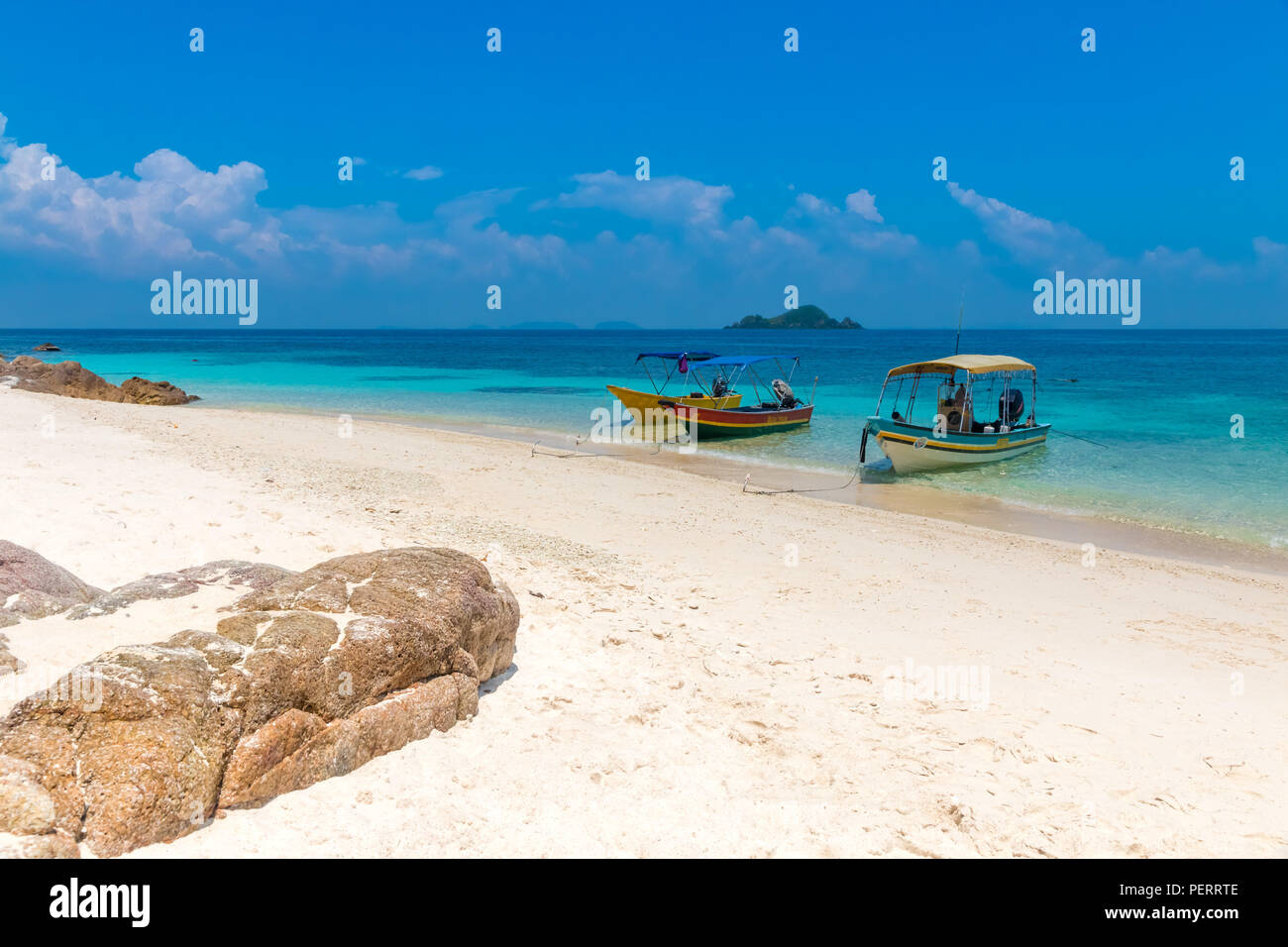 Three tourist boats anchoring on a white powdery sandy beach, a blue sky and a small island on the horizon makes it a gorgeous scene of the... Stock Photo