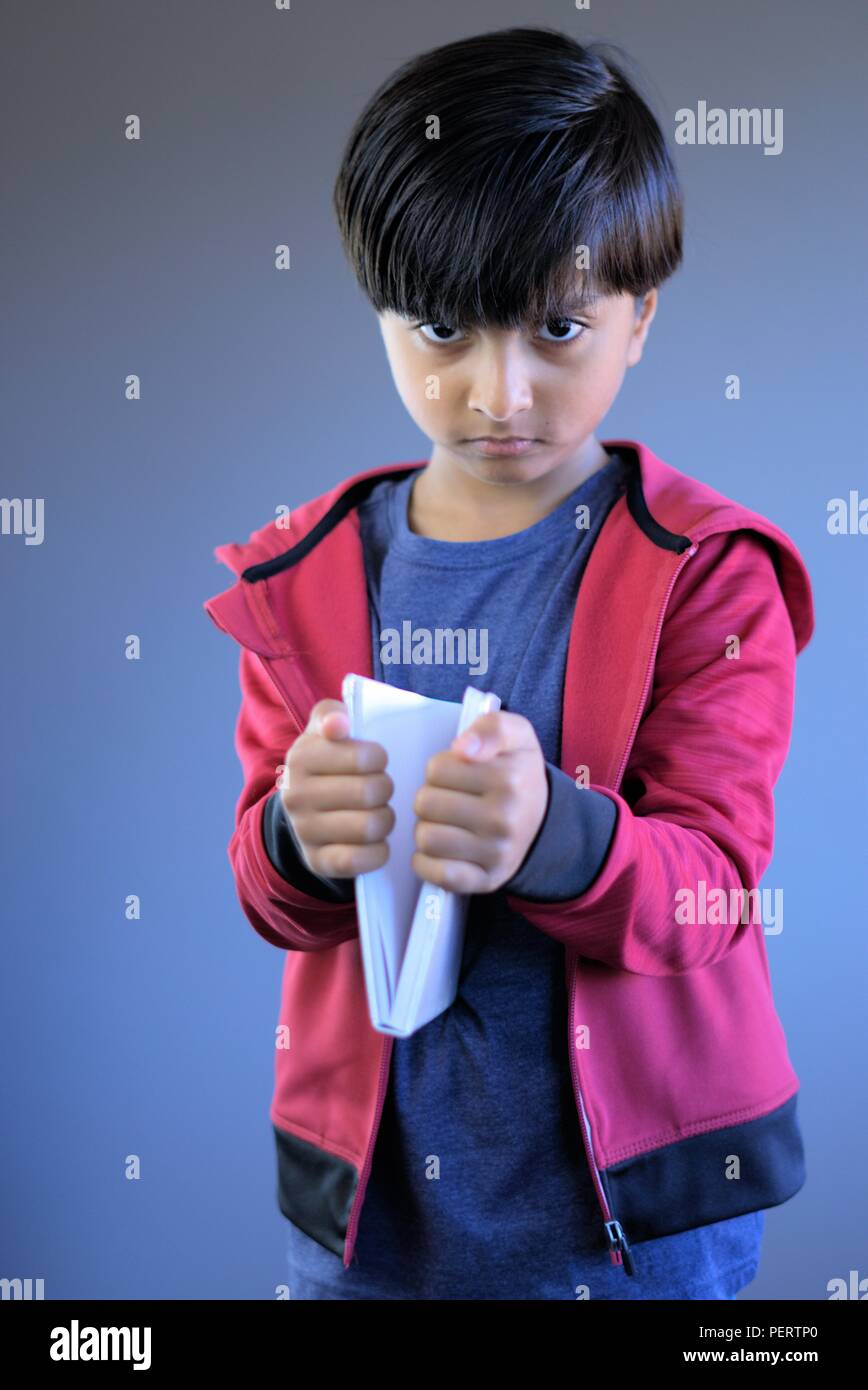 Portrait of angry kid holding book. Aggressive kid with book. Concept of child not happy studying or with education. Stock Photo