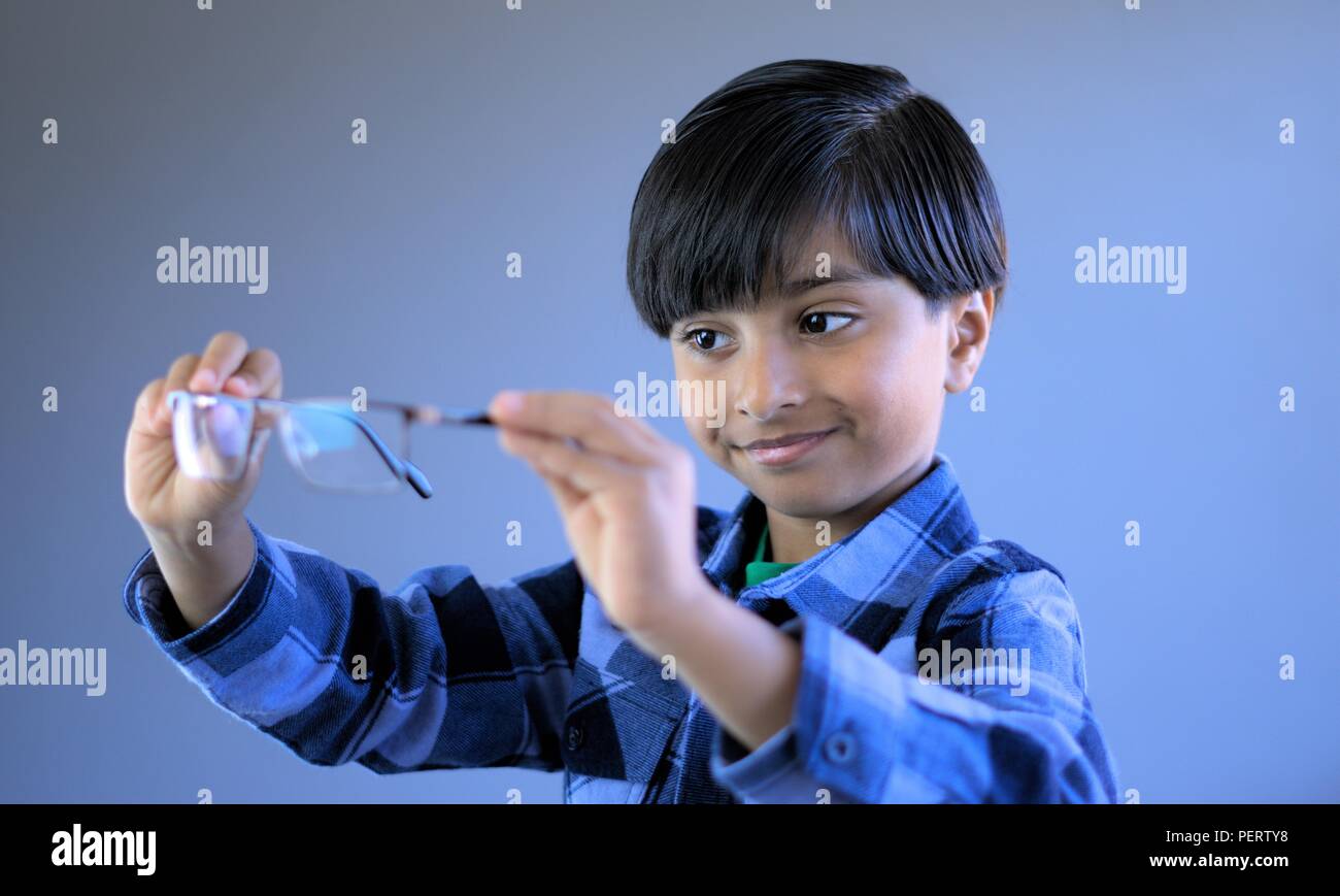 Smiling Kid checking eye glasses before wearing them. Child in act of wearing glasses. Subject looking at glasses. Stock Photo