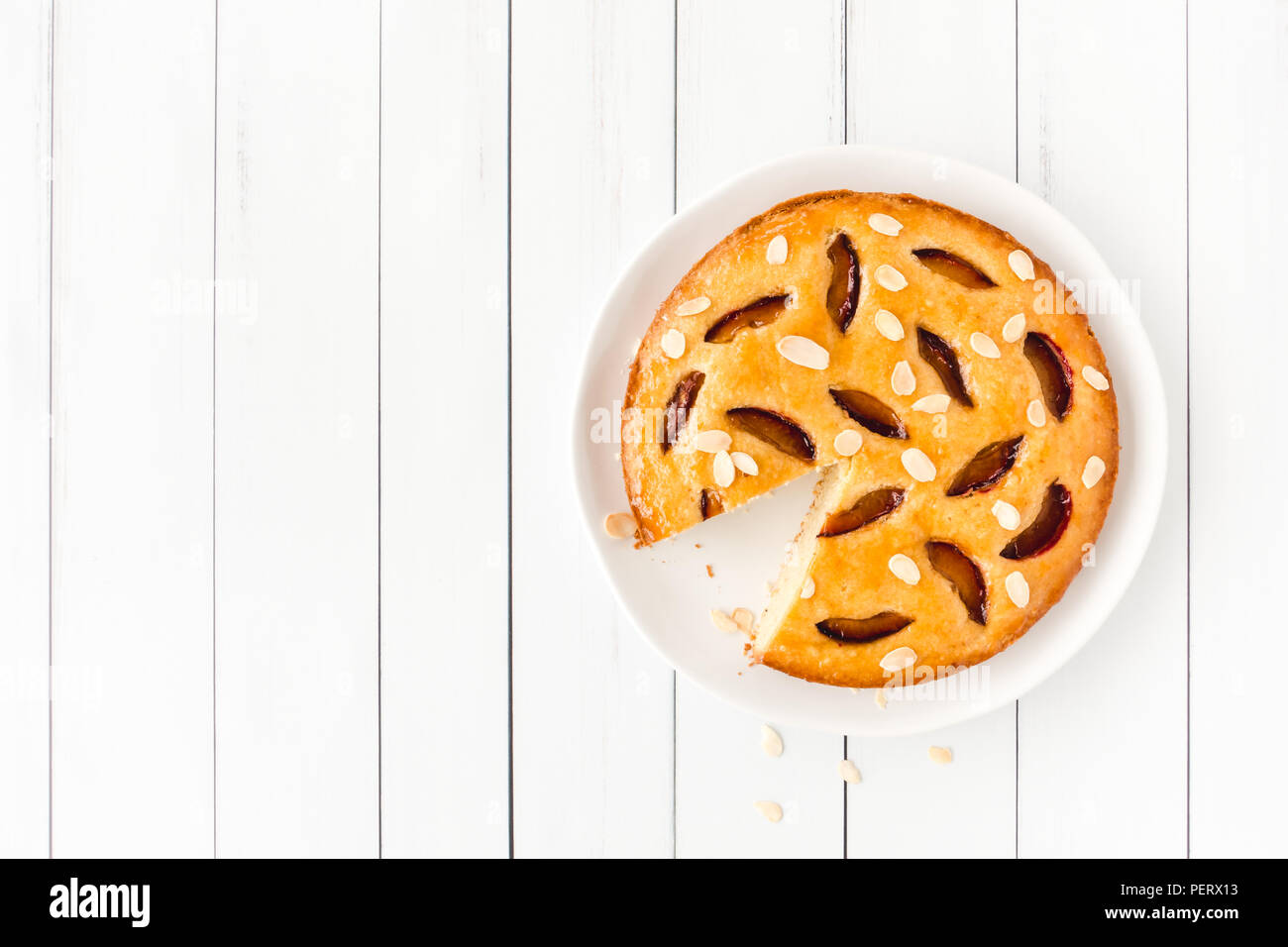 Cut homemade plum cake on porcelain cake plate and white wood planks. Stock Photo
