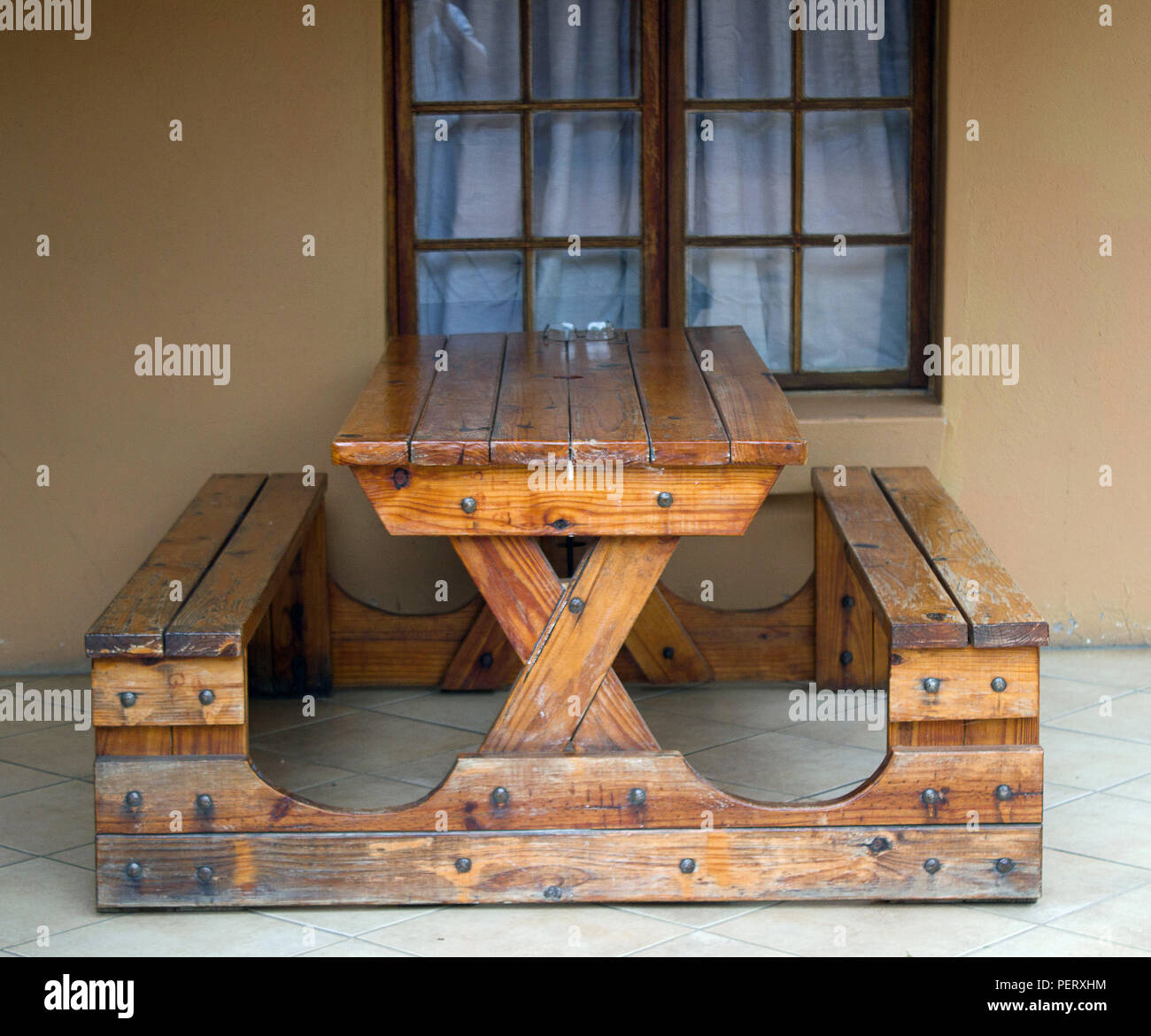 Sturdy wooden table with two seats attached as one unit standing on stoep against a window Stock Photo