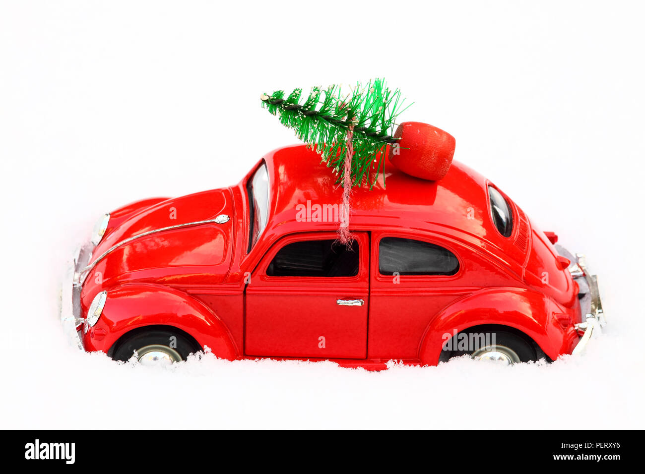 Red toy volkswagen beetle car with a christmas tree tied to the roof on