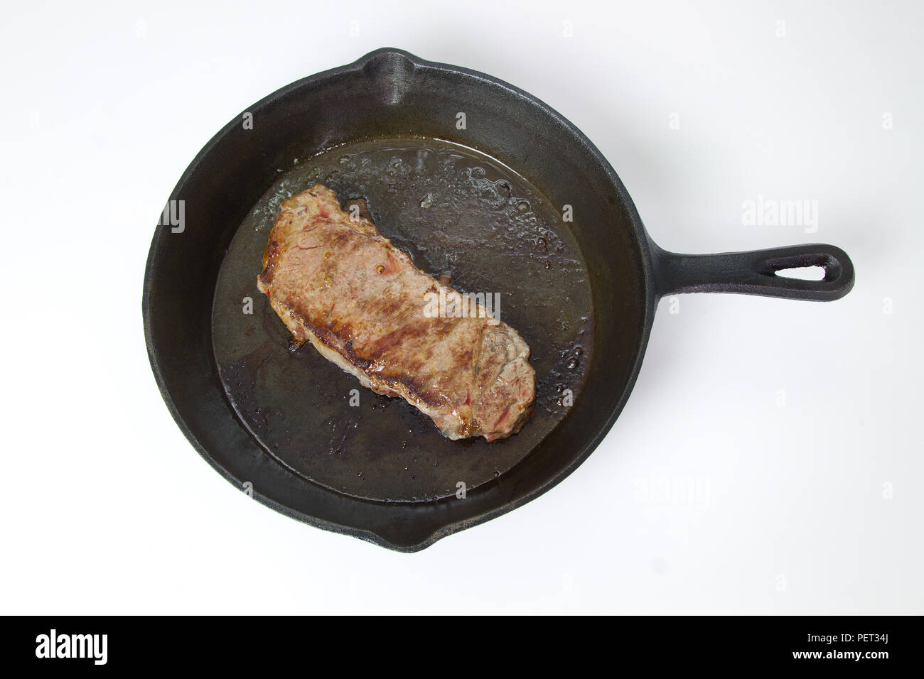 Beef Steak frying in a cast iron skillet isolated on white background with room for text Stock Photo