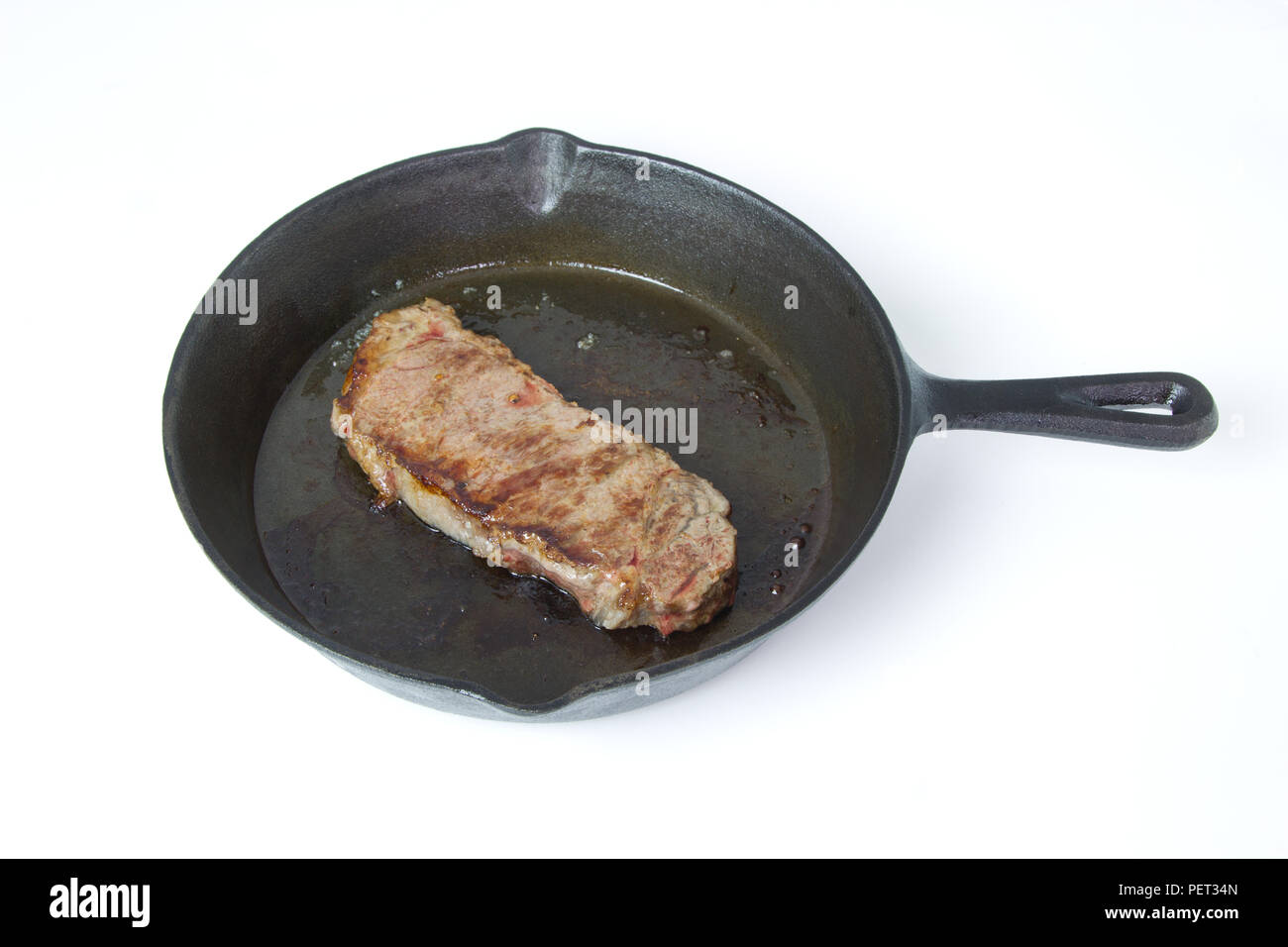 Beef Steak frying in a cast iron skillet isolated on white background with room for text Stock Photo
