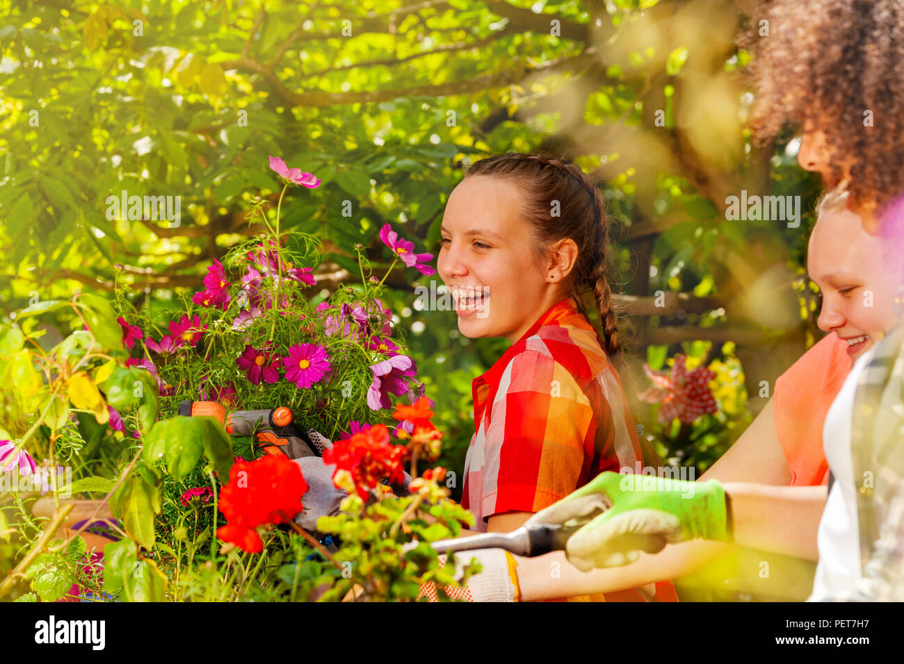 Portrait of laughing girl working in the garden with friends, watering plants using hand sprinkler Stock Photo