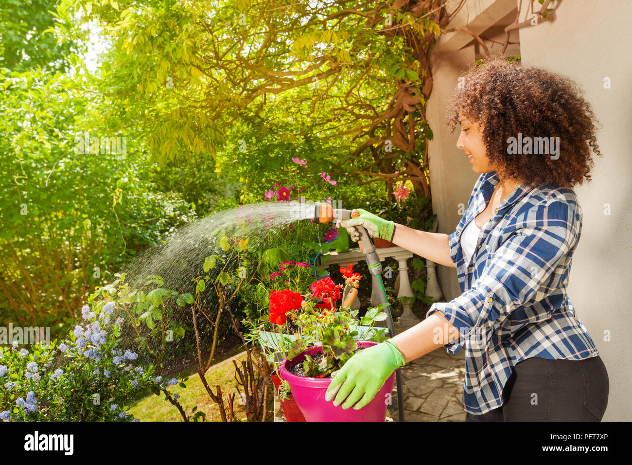 Side view portrait of teenage African girl watering plants using garden hose and hand sprinkler Stock Photo