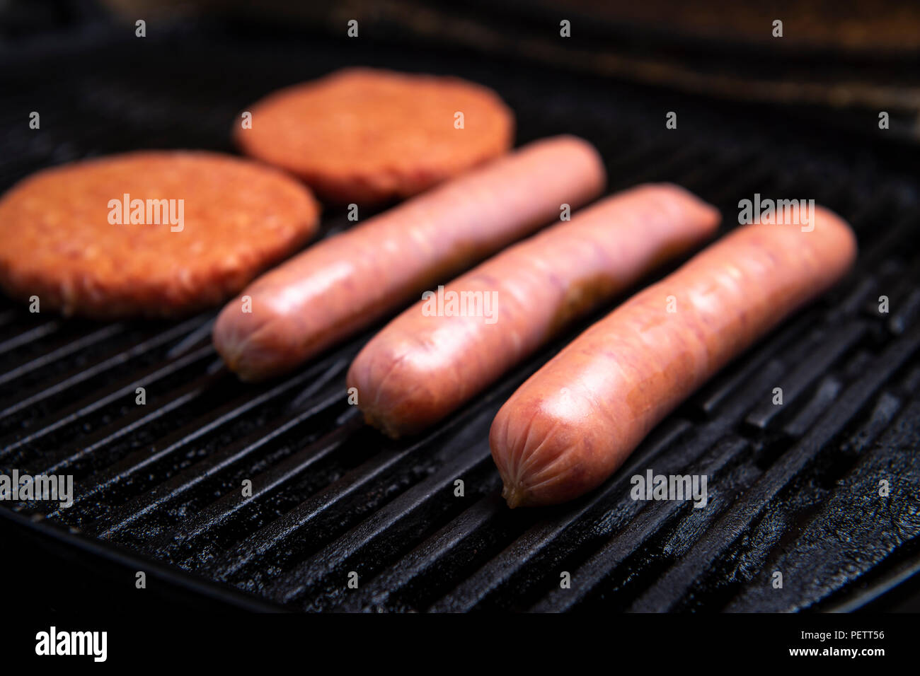 Fresh uncooked barbecue sausages, burgers and bread ready to be grilled, sitting on a grill Stock Photo