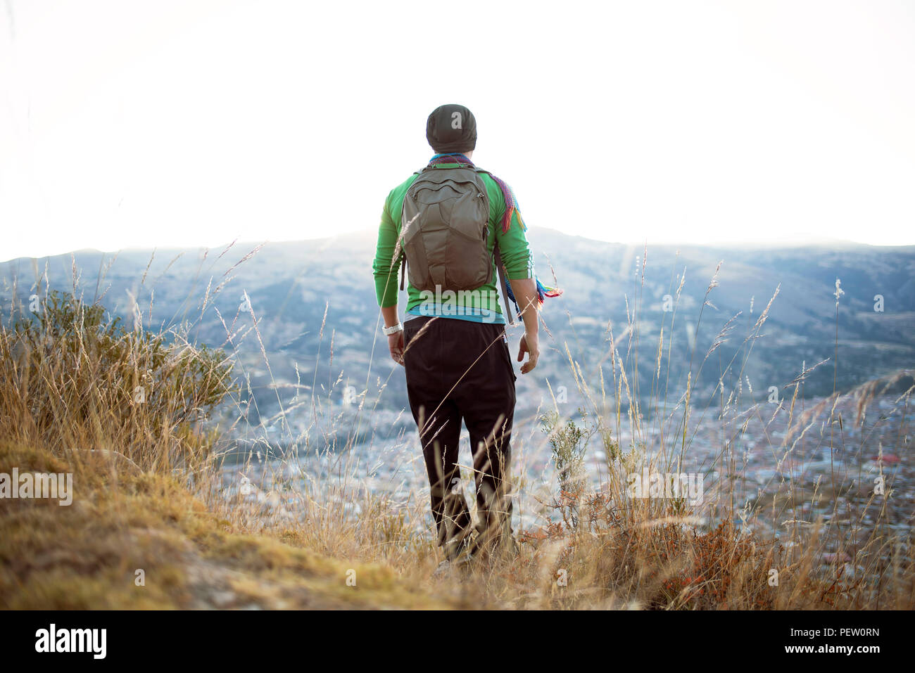 Sporty backpacker man from behind walking downhill with scenic city views. Trekking in nature, wanderlust, outdoor lifestyle. Huaraz, Peru. Jul 2018 Stock Photo