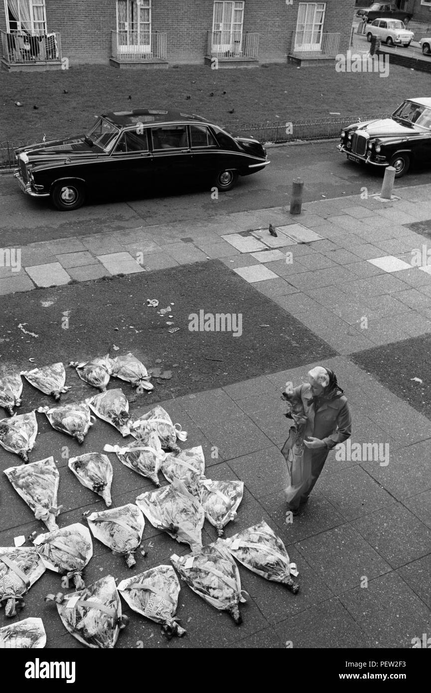 Funeral 70s UK. Hoxton east London woman bringing flowers and to pay her respect. Many bouquets of flowers left on the pavement area outside a block of flats. 1970s England. HOMER SYKES Stock Photo