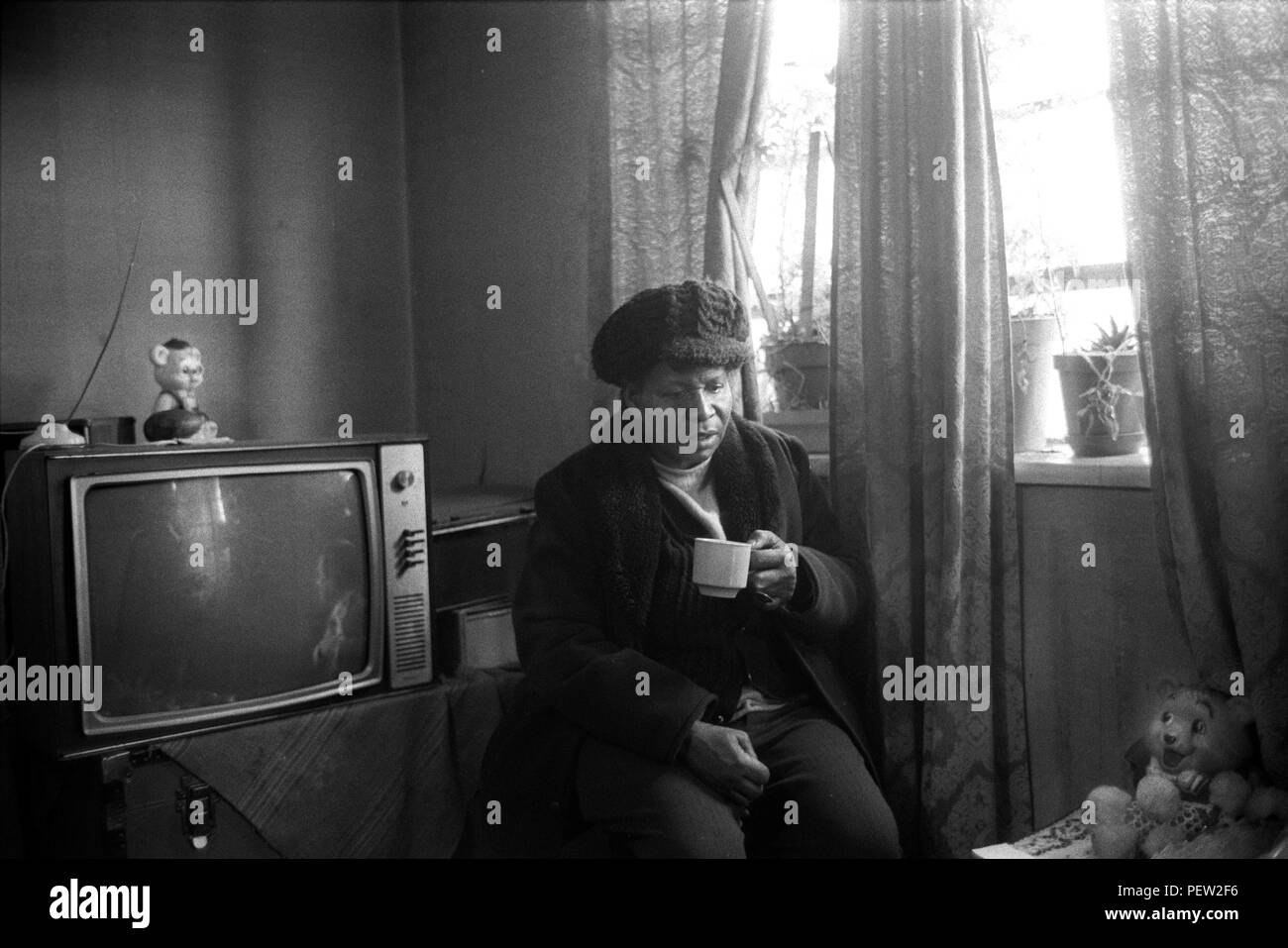 East End London 1970s, poverty in Britain, an elderly black British woman in her council estate flat on the Stonebridge Estate.  Isolated and living alone in a single room plus small kitchen and bathroom. All in very bad condition, the flat is damp and very cold, she is dressed in her hat and coat and drinks a cup of tea to keep warm. Haggerston, East London, England 1978. 70s UK HOMER SYKES Stock Photo