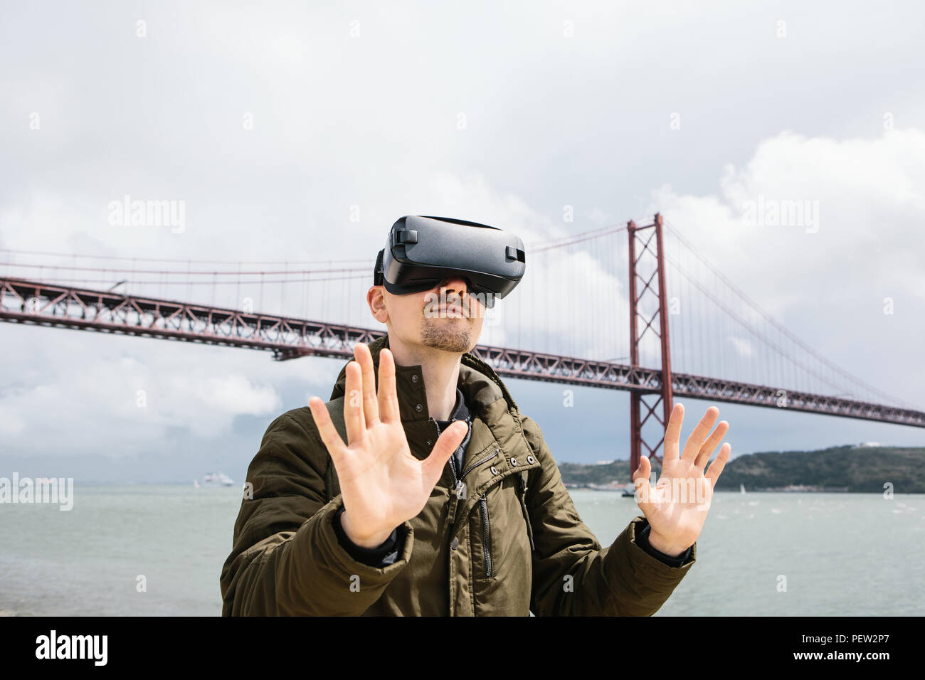 A man uses virtual reality glasses. The concept of virtual travel. 25th of April bridge in Lisbon in the background. The concept of modern technologies and their use in everyday life. Stock Photo