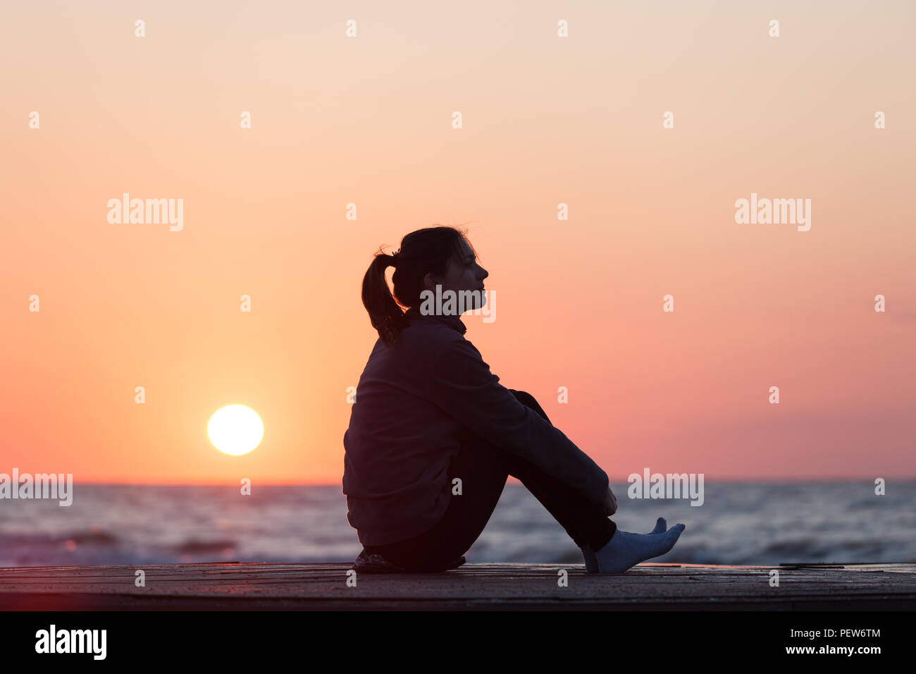 Lonely girl sitting on the sunrise beach. Woman silhouette over sunrise sky Stock Photo