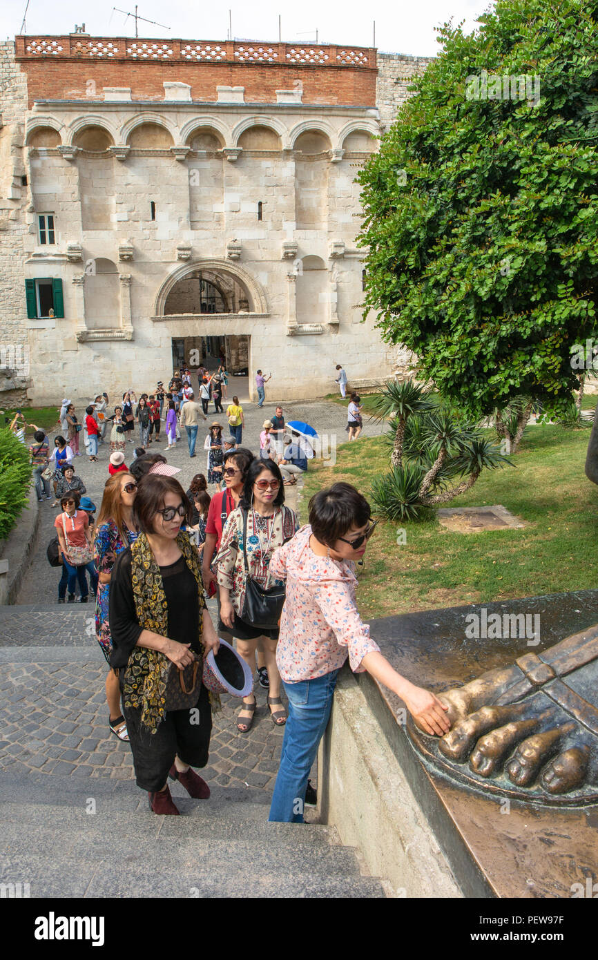 Split, Croatia. Asian female tourist is rubbing the toe of the Statue of Grgur Ninski, Bishop Gregory of Nin - it is said to bring good luck. Stock Photo
