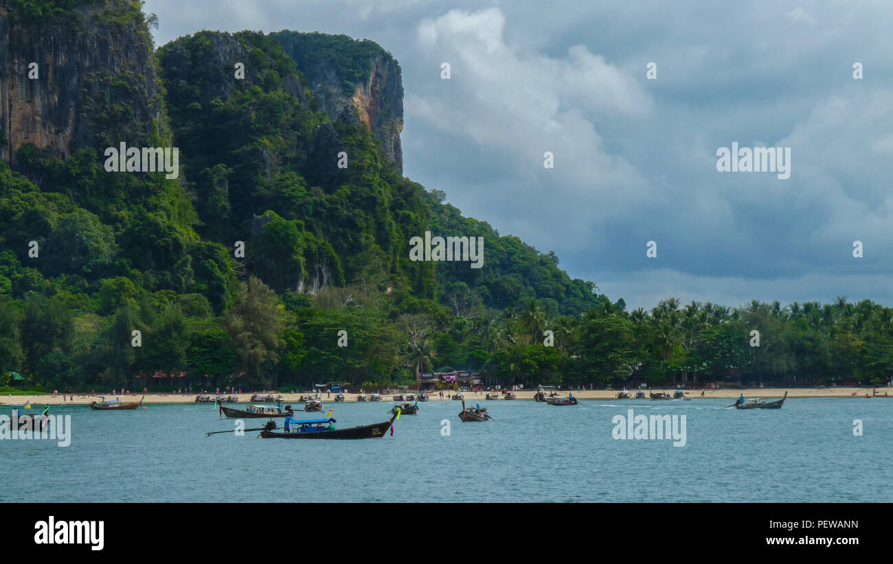 Landscape view of one of the beaches of the Krabi province, in Thailand, with dozens of long-tail boats on the water, and limestone cliffs in the back Stock Photo