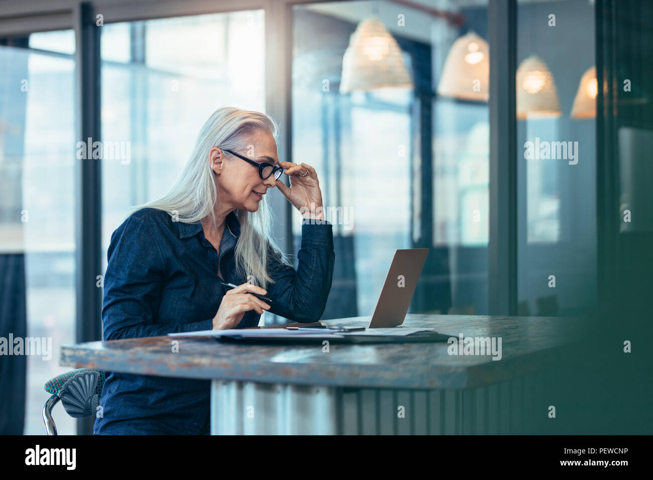 Senior business woman working on laptop in office. Caucasian mature female looking at laptop computer while sitting at her desk. Stock Photo