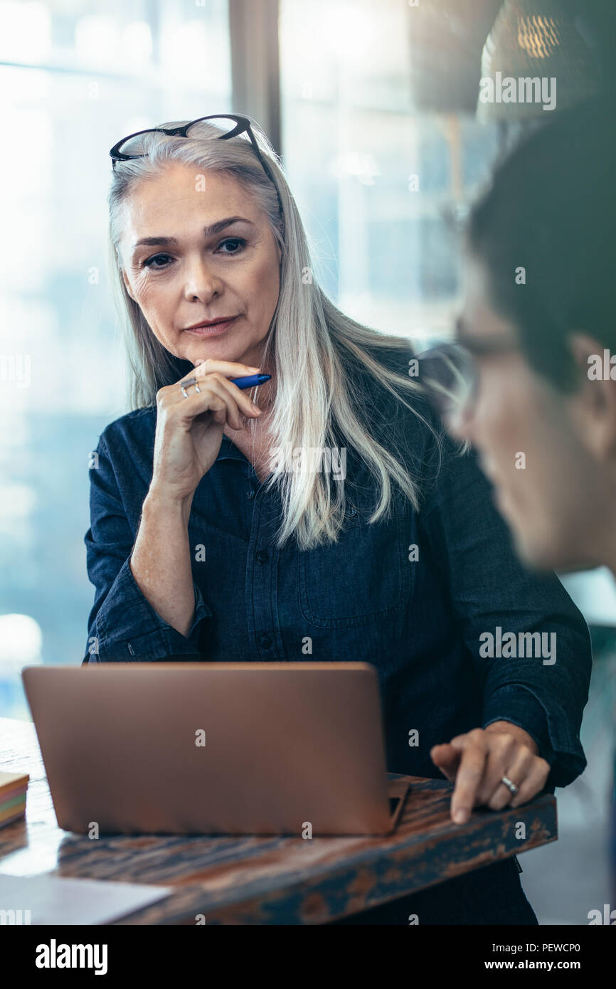 Senior business woman listening to her male colleague during meeting in office. Mature female paying attention to the discussing in meeting. Stock Photo