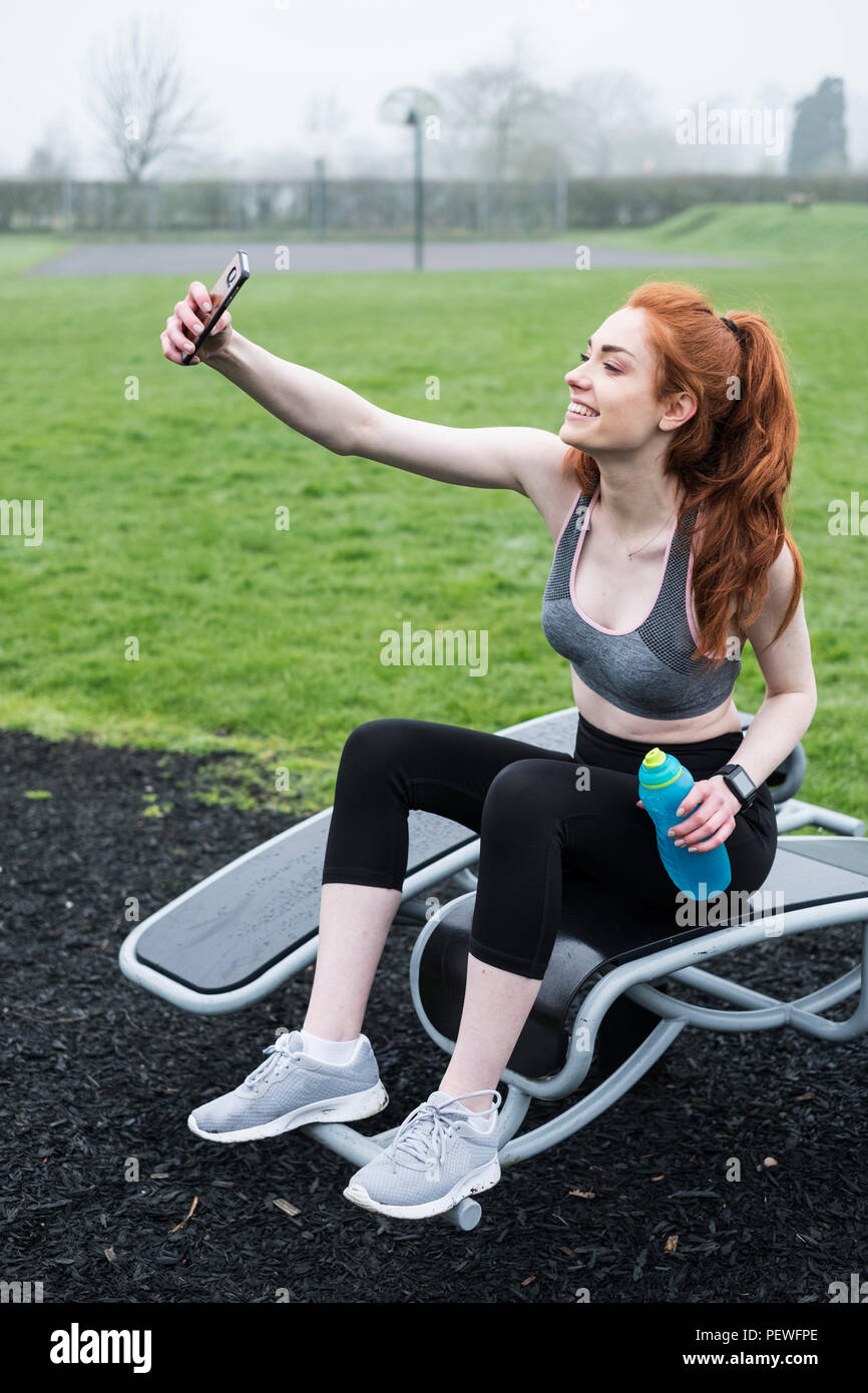 Smiling young woman with long red hair wearing sportswear, exercising outdoors. Stock Photo