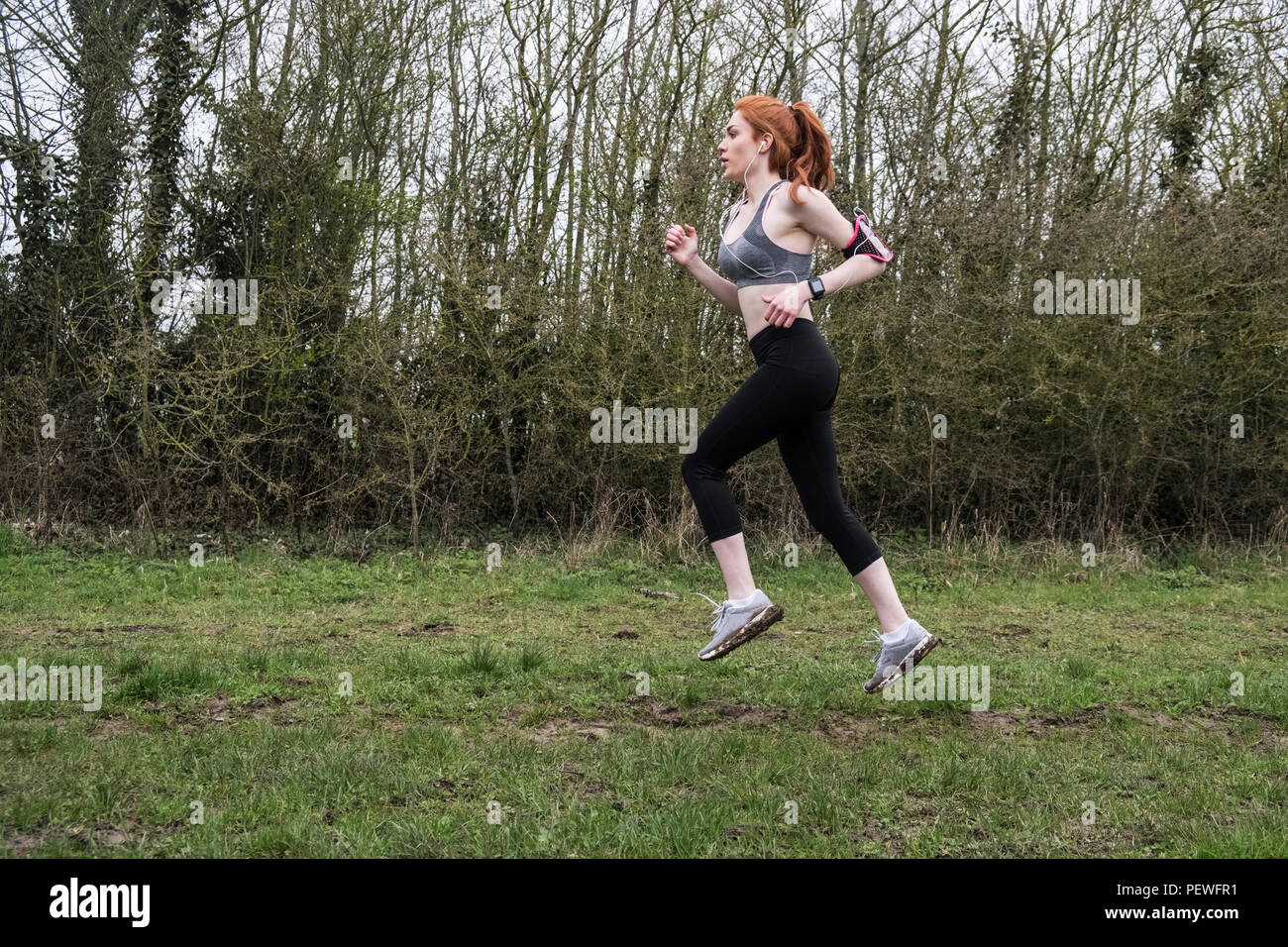 Young woman with long red hair wearing sportswear, exercising outdoors. Stock Photo