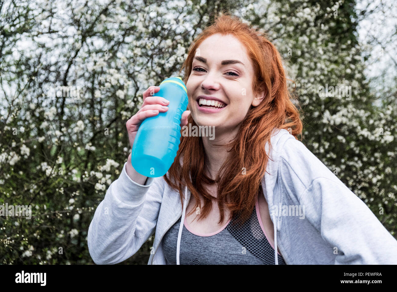 Smiling young woman with long red hair wearing sportswear, exercising outdoors, looking at camera. Stock Photo