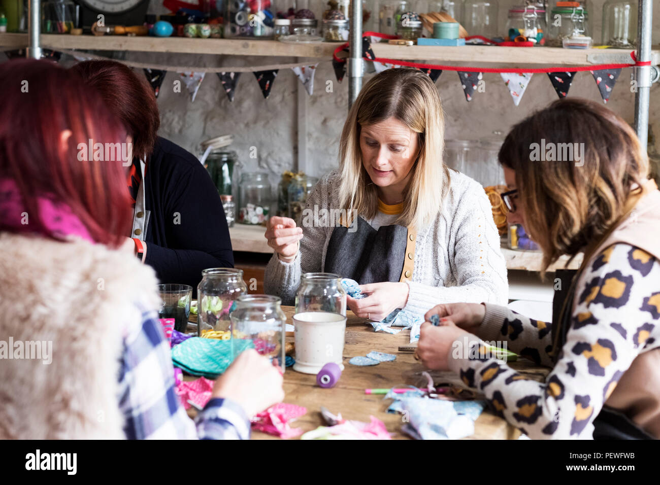 Group of women sitting around a table in a workshop, making fabric flowers. Stock Photo