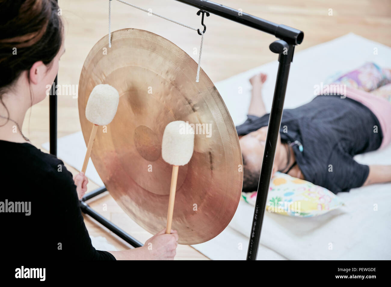 Woman striking a large gong wit soft drumsticks during a sound therapy