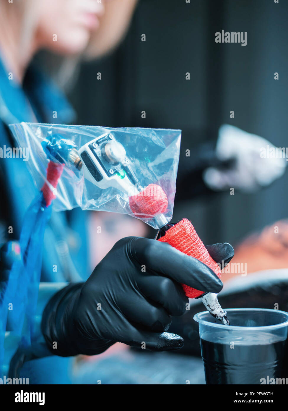 Female tattoo artist dipping the machine needle into disposable ink cup