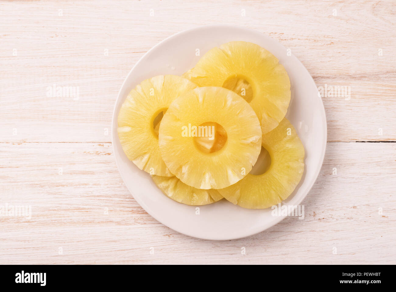Top view of canned pineapple slices on plate on wooden background Stock Photo