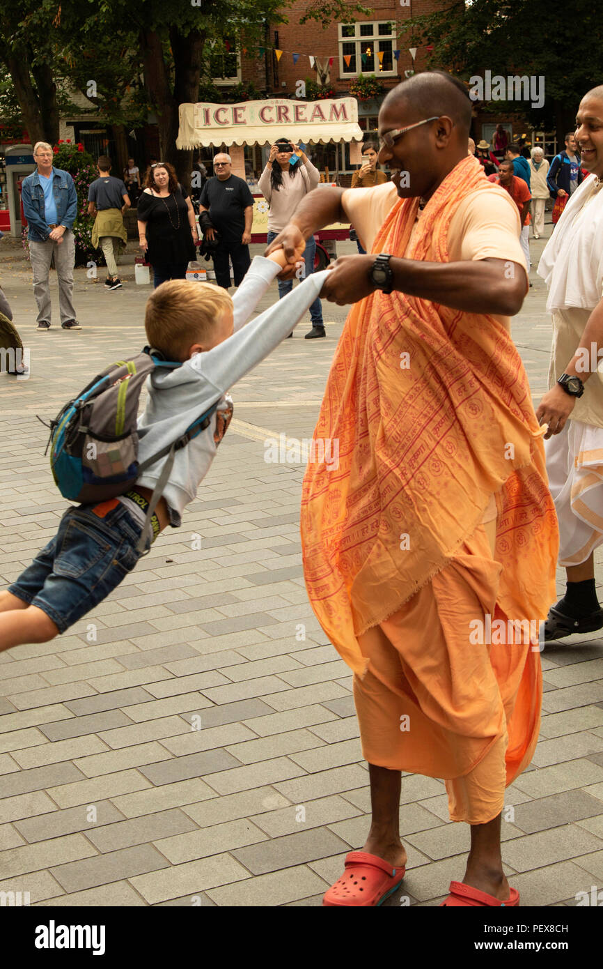 Male Hare Krishna member swinging young boy in Kings Square, York, North Yorkshire, England, UK. Stock Photo